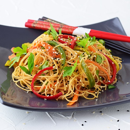 Black plate of cold noodle salad with red and black chopsticks